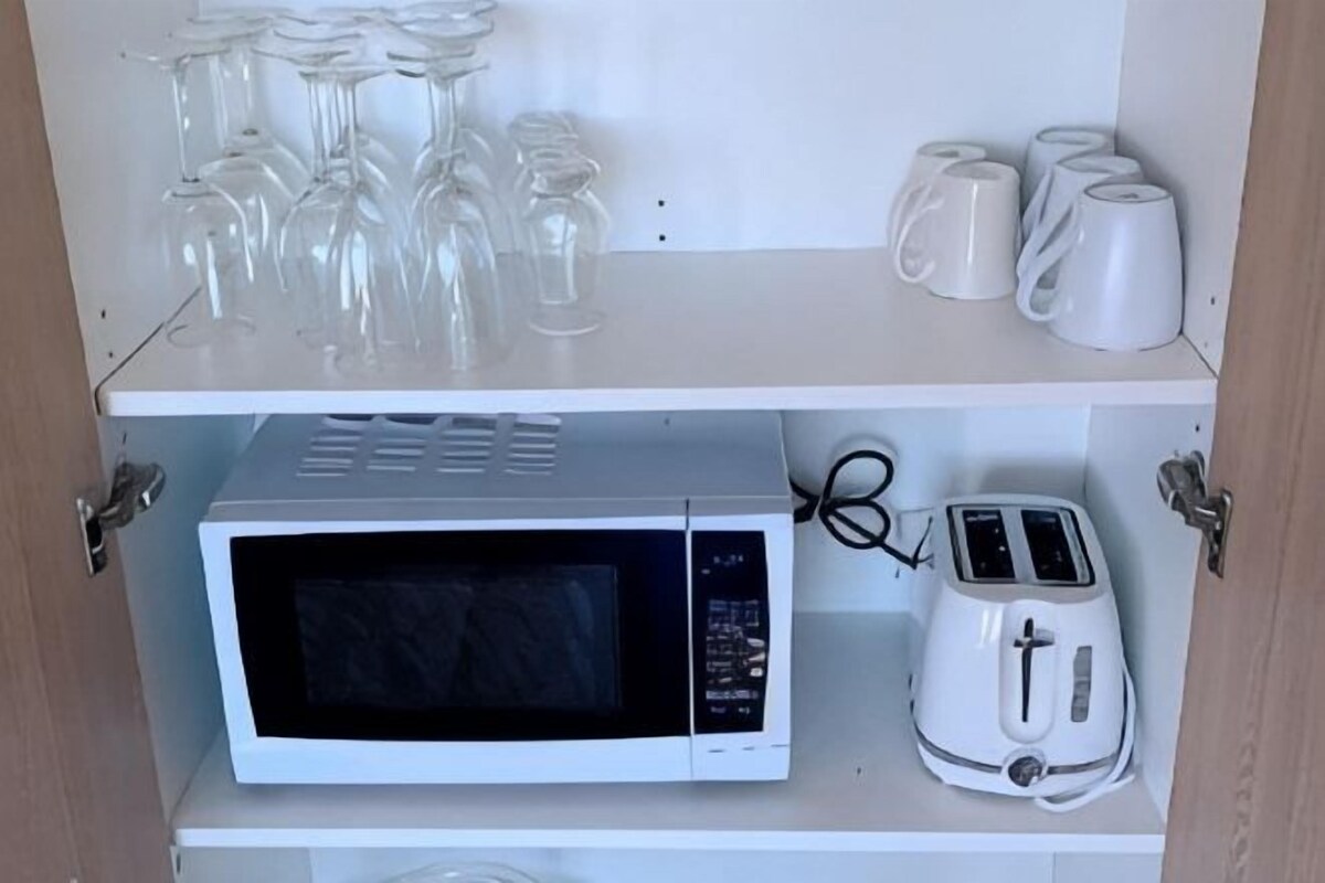 A kitchen with a microwave, toaster, and glassware on shelves.
