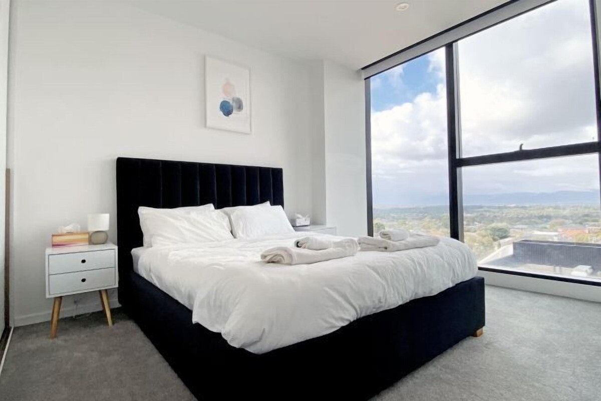 Un dormitorio moderno con un ventanal grande, un cabecero negro y una cama bien hecha.