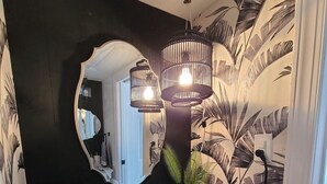 Un baño con pared negra, un espejo, un lavamanos, un perchero para toallas y una planta en maceta.