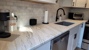 Una cocina moderna con encimera de mármol, lavavajillas integrado, cafetera, dispensador de toallas de papel y horno tostador.