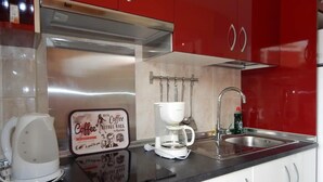 A kitchen with red cabinets, a stainless steel range hood, a coffee maker, and a coffee pot.