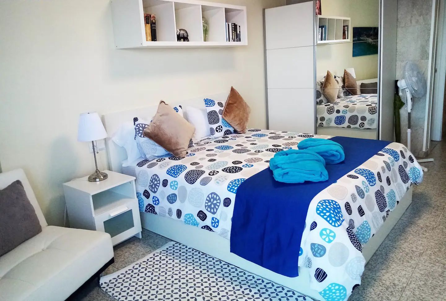 Een slaapkamer met een bed, nachtkastjes, een spiegel en een garderobe.