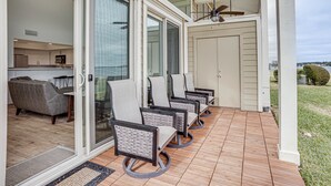 Un patio con cuatro sillas, un ventilador de techo y un gran ventanal corredizo que da a una cocina.