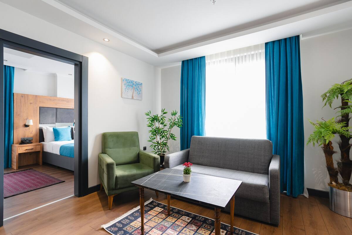 Ein modernes Hotelzimmer mit einem Bett, einem grünen Sessel, einem grauen Sofa und einem kleinen Tisch mit einer Pflanze.