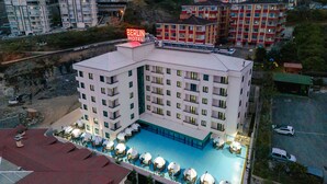 Hotel amb diverses plantes, piscina i gandules, i zona d'aparcament.