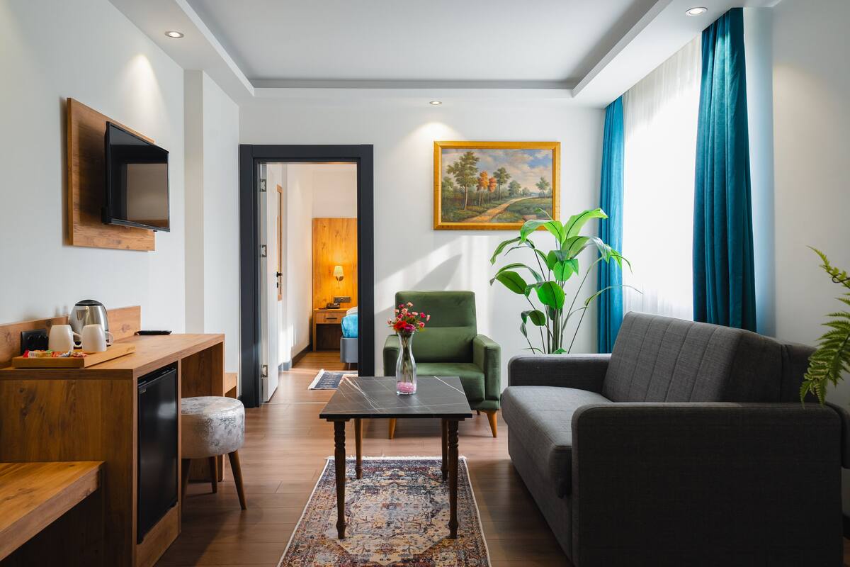 Ein modernes Wohnzimmer mit einer Couch, einem Couchtisch, einem an einer Holzplatte befestigten Fernseher, einem grünen Sessel und einem Gemälde an der Wand.