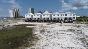 Un bien immobilier situé en bord de mer, composé de plusieurs bâtiments blancs, dont certains sont surélevés sur des piliers, et avec une route visible au loin.