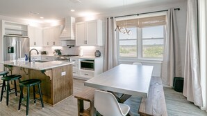 Une cuisine moderne avec des meubles blancs, un grand îlot central doté de tabourets et une vue sur la verdure à l’extérieur.