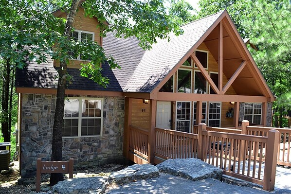 A lodge with a stone facade, a wooden deck, and a sign indicating its name. - L004, 4Br, 4Ba Refreshing Roark Creek Cabin (Branson West)