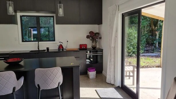 Una cocina moderna con una isla grande, armarios oscuros y un puerta corrediza de vidrio que da a un patio.