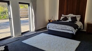 Un dormitorio con cama, alfombra blanca, cabecera de madera y vista a través de un ventanal.