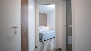 A narrow hallway leading to a bedroom with a bed, a nightstand, and a wall-mounted light fixture. - WePuglia – Appartamento GiuGio (Polignano a Mare)