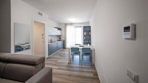 A modern living room with a sofa, a dining area with a table and chairs, a kitchen with cabinets, and a bookshelf. - WePuglia – Appartamento GiuGio (Polignano a Mare)