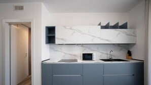 A modern kitchen with grey cabinets, a white marble backsplash, and a microwave. - WePuglia – Appartamento GiuGio (Polignano a Mare)
