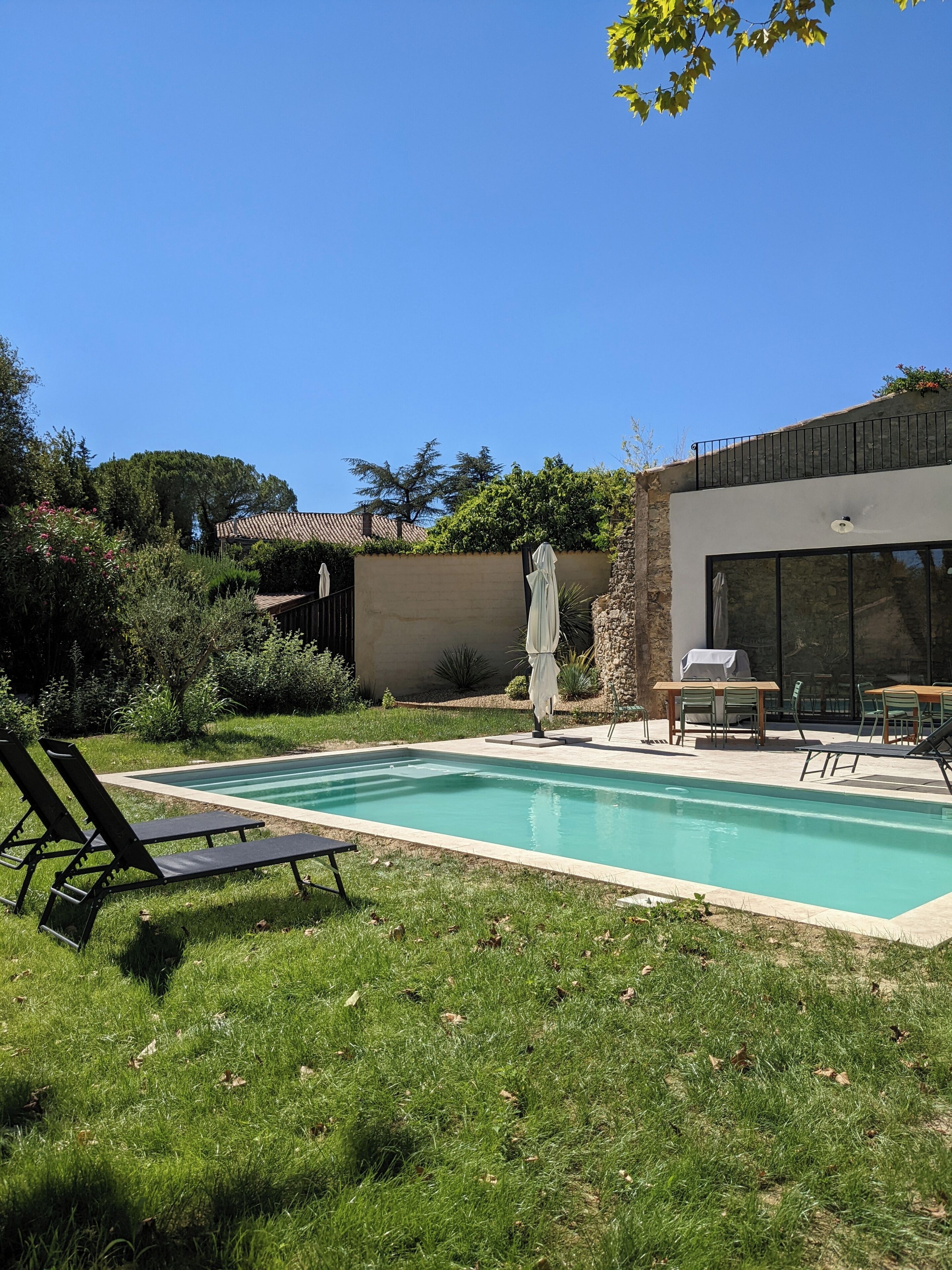 A modern outdoor pool area with lounge chairs, a dining table, and a covered patio.