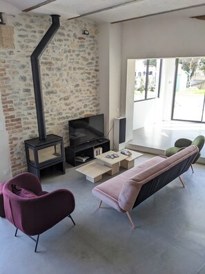 A modern living room with a stone wall, a black fireplace, a TV, and a sofa.