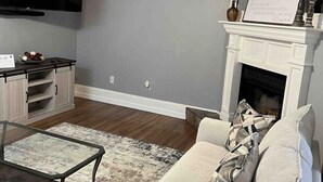 A living room with a flat-screen TV, a ceiling fan, a fireplace, a sofa, and a coffee table. - Location!! Minutes from L’Auberge/LSU/DOWNTOWN (Baton Rouge)