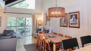 Een ruime woonkamer met een houten eettafel, comfortabele zitplaatsen en een groot raam met uitzicht op de omgeving.