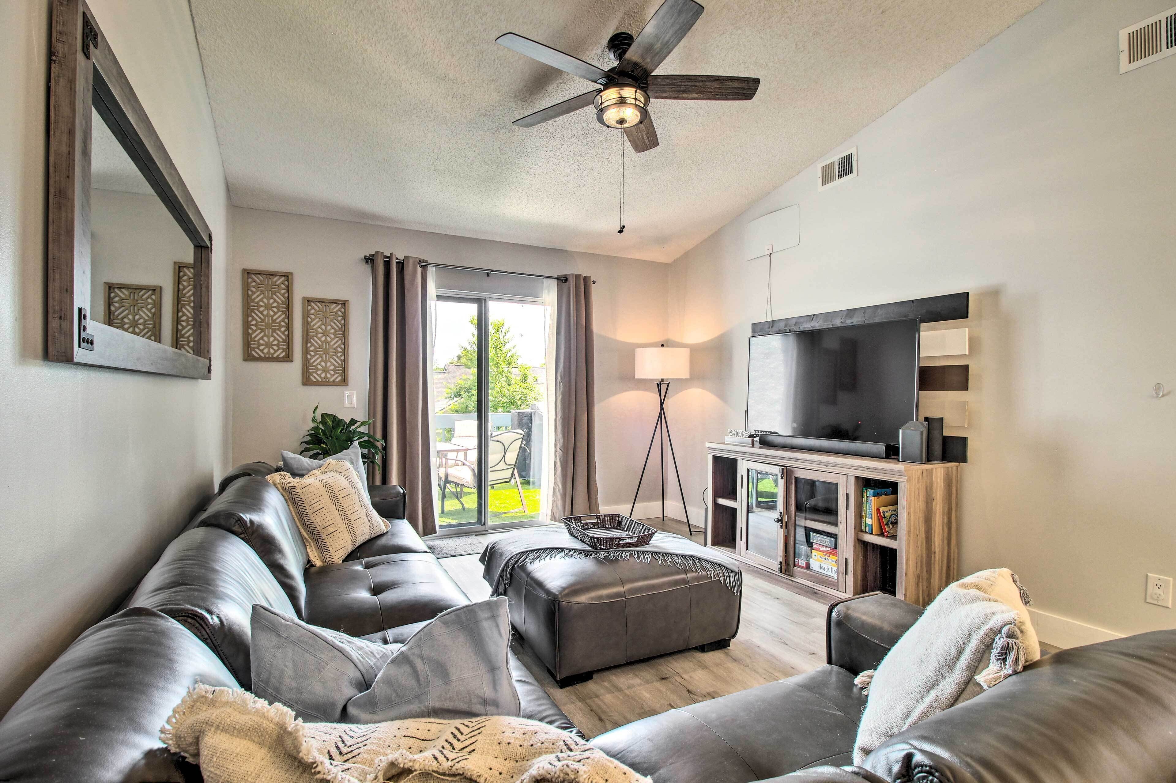 A modern living room with a leather sofa, a flat-screen TV, a ceiling fan, and a large window with curtains.