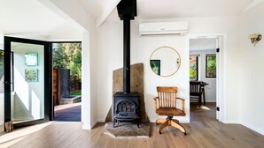 A modern interior with a wood-burning stove, a wooden chair, and a round mirror on the wall.