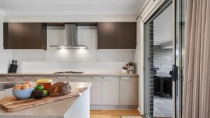 A modern kitchen with a central island, a stove, and a large window. - Modern Farm Stay - South Coast (Yatte Yattah)