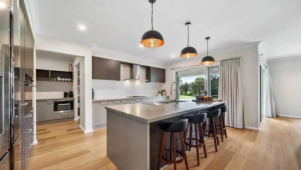 A modern kitchen with a central island, bar stools, pendant lighting, and a view of the outdoors. - Modern Farm Stay - South Coast (Yatte Yattah)