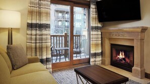 A living room with a sofa, a table, a fireplace, and a TV mounted on the wall. - Spring Ski Week in the Canyons- Ski In/Ski Out (Park City)