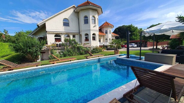 A swimming pool with lounge chairs, a large house with a red roof, and a well-maintained garden. - Ferienwohnung mit Pool und Tischtennisplatte (Siófok)