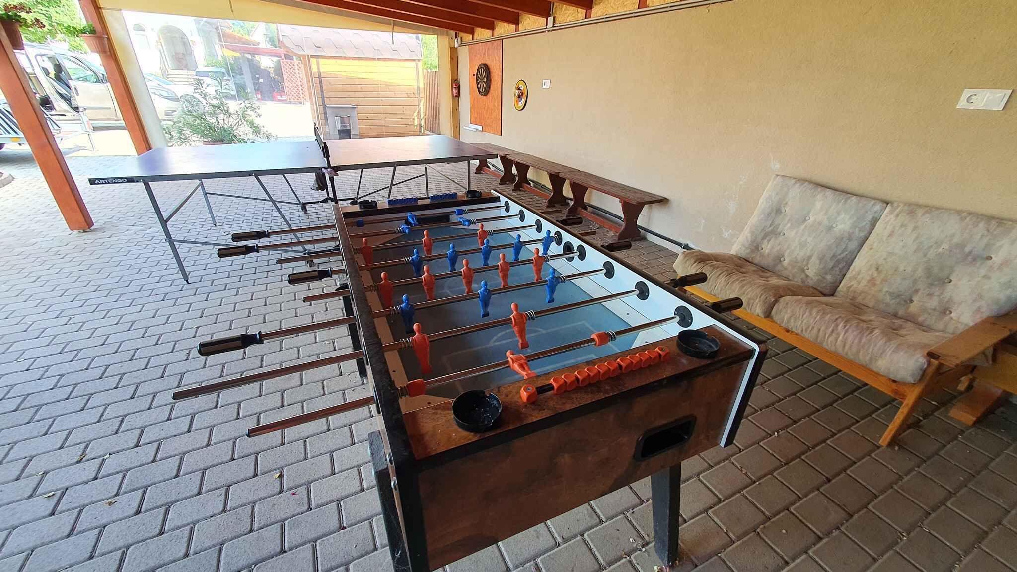 A foosball table in an outdoor area with a brick floor, a sofa, and a wooden table.
