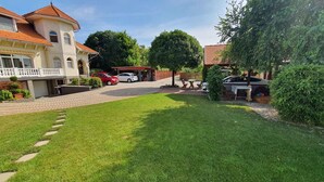 A courtyard with a paved walkway, a lawn, and a building with a red-tiled roof. - Ferienwohnung mit Pool und Tischtennisplatte (Siófok)