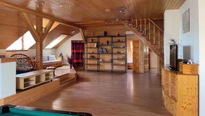 A spacious loft with a high ceiling, wooden beams, a built-in bookshelf, a pool table, and a staircase leading to an upper level. - Ferienwohnung mit Pool und Tischtennisplatte (Siófok)