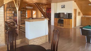 A spacious loft with a high ceiling, wooden beams, a central island with seating, a pool table, and a staircase leading to an upper level. - Ferienwohnung mit Pool und Tischtennisplatte (Siófok)