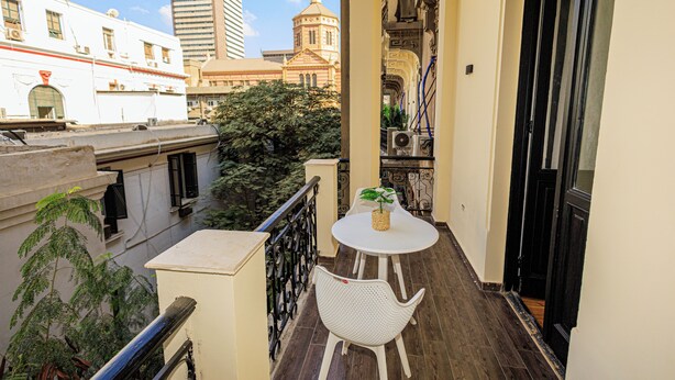 A balcony with a white table and chair, a potted plant, and a view of city buildings.