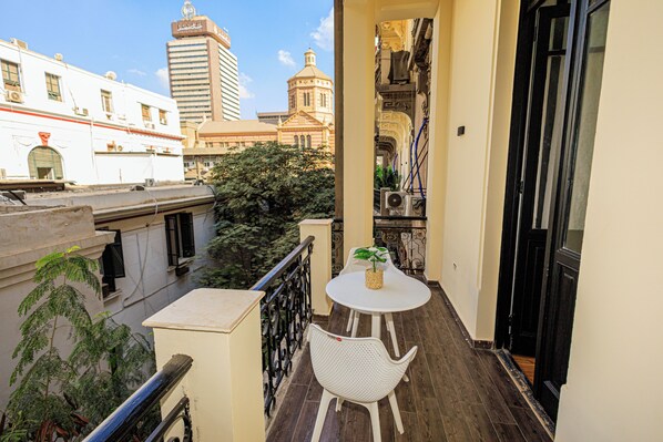 A balcony with a white table and chair, a potted plant, and a view of city buildings.