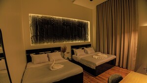 A hotel room with two beds, a large wall-mounted artwork, a wooden floor, and a view of the outdoors.