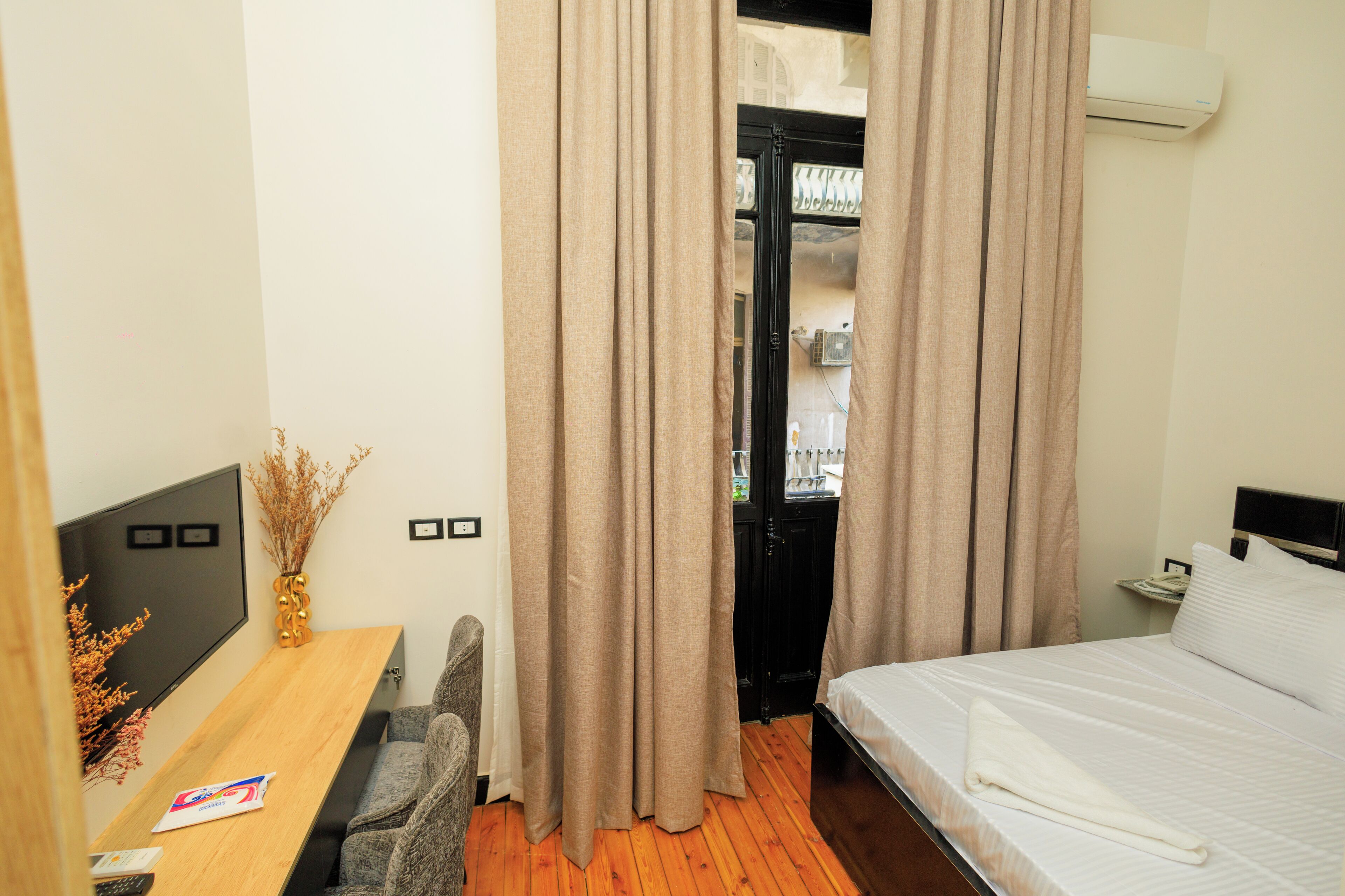 Een hotelkamer met een houten bureau, een bed en beige gordijnen.