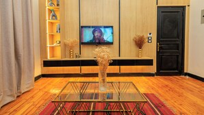 A hotel lobby with a television on the wall, a wooden reception desk, a glass coffee table, and a door.