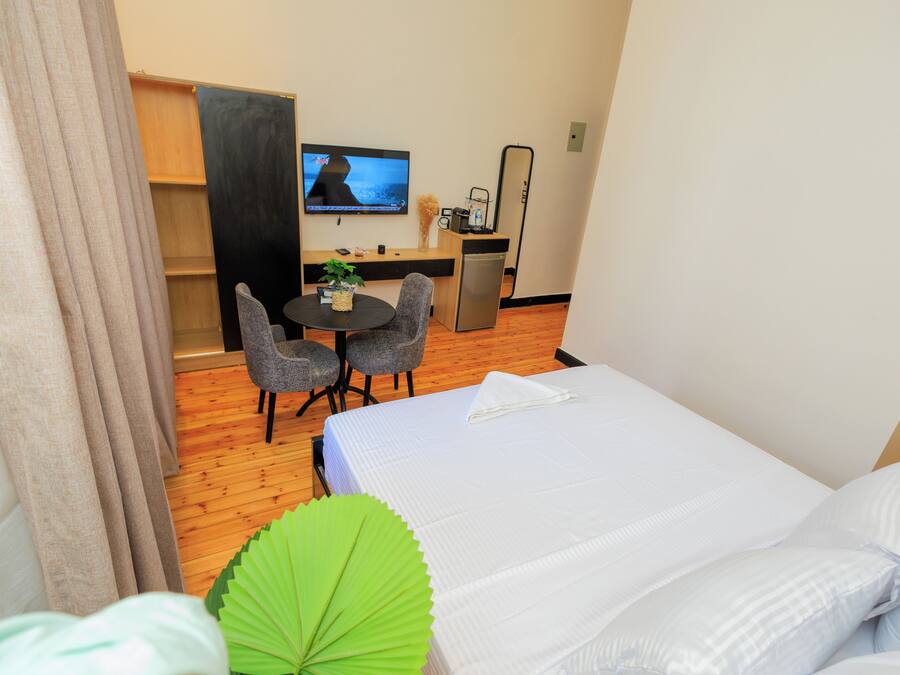 A hotel room with a bed, a desk with a chair, a television, and a small kitchenette.