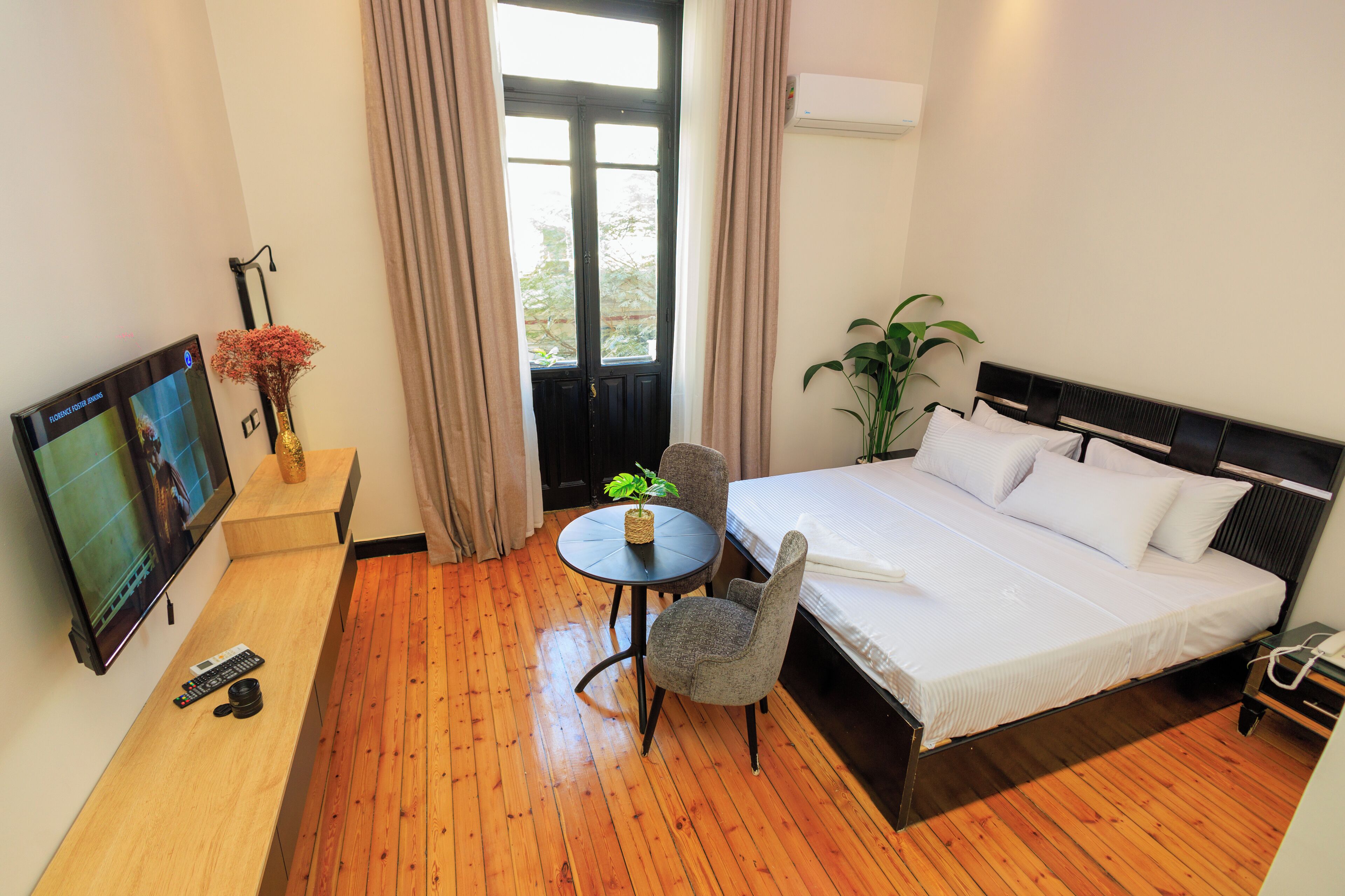 Ein Hotelzimmer mit Bett, Fernseher, kleinem Tisch mit Pflanze und Stuhl.