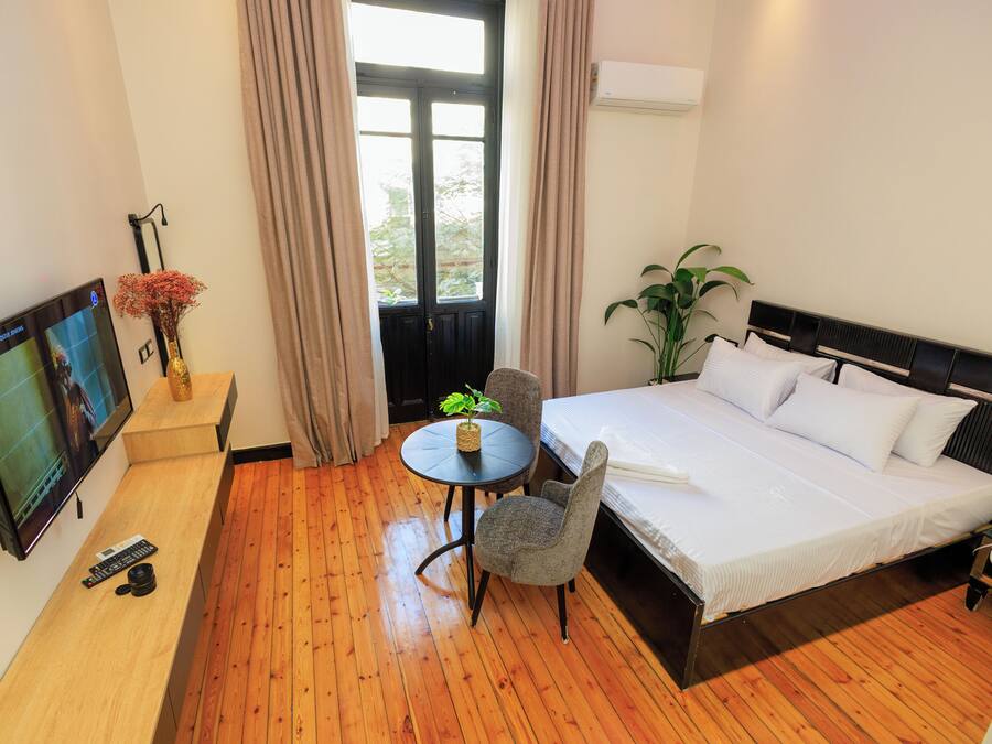 Ein Hotelzimmer mit Bett, Fernseher, kleinem Tisch mit Pflanze und Stuhl.