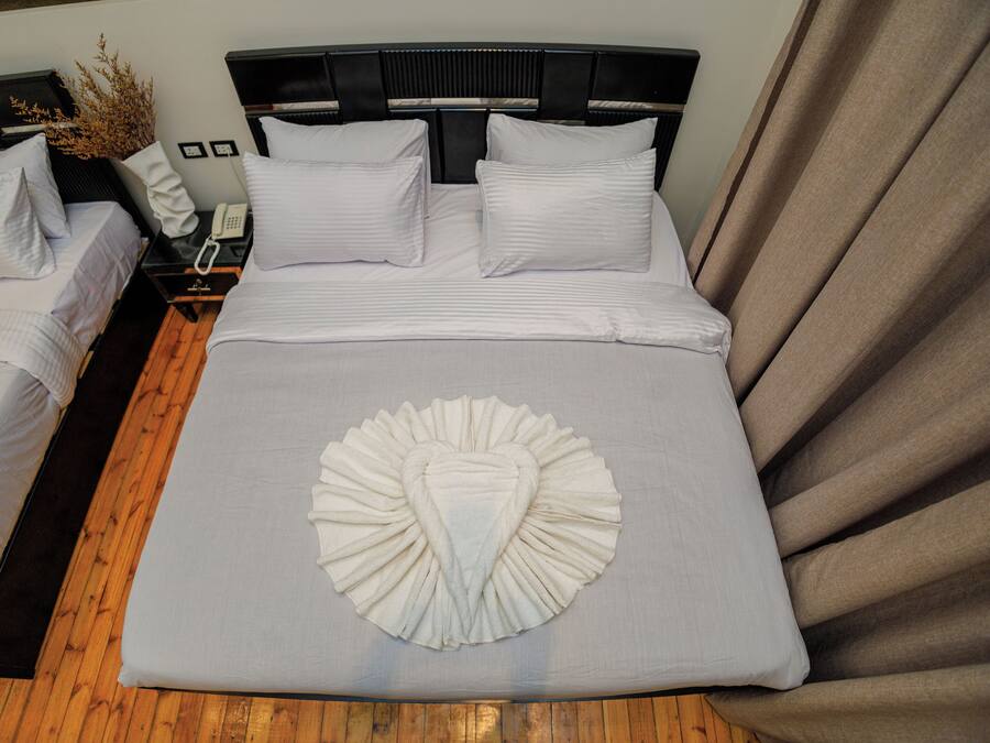 Habitación de hotel con dos camas, suelo de madera, un cojín decorativo grande, un teléfono en la mesita de noche y una cortina.