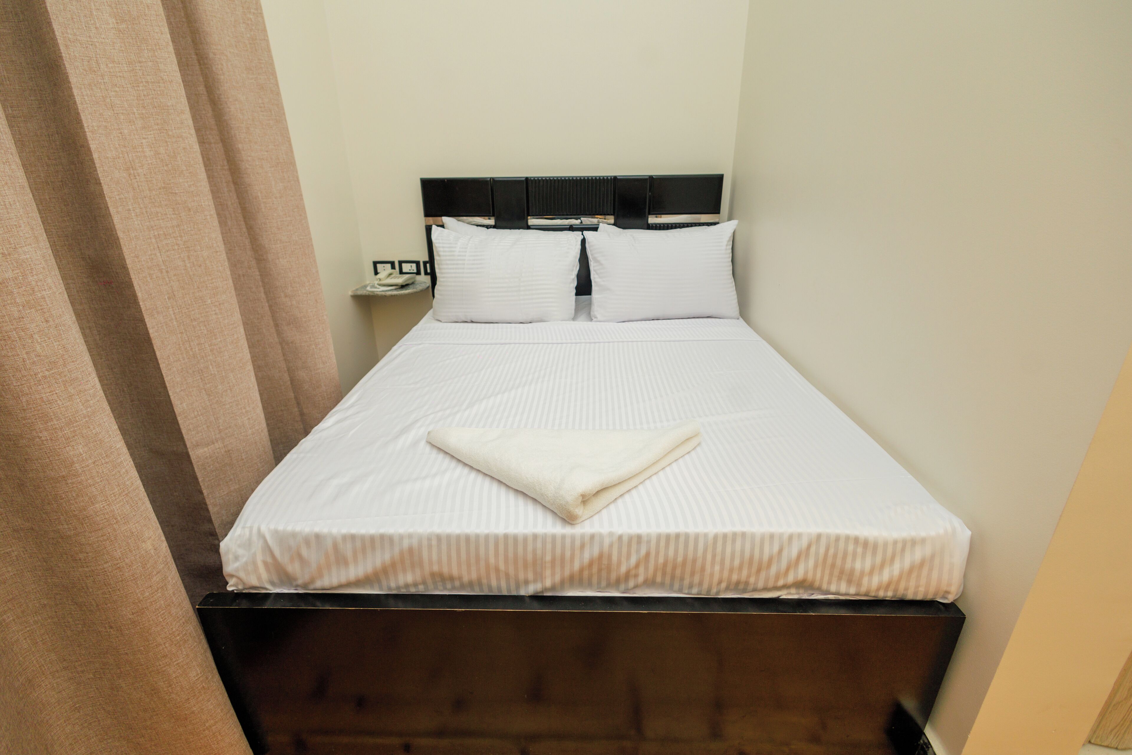 A single bed with a wooden headboard, white bedding, and a folded blanket on the bed.