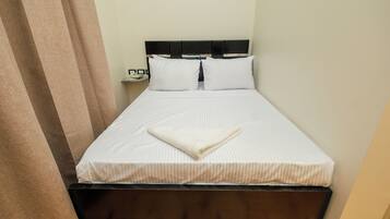 A single bed with a wooden headboard, white bedding, and a folded blanket on the bed.