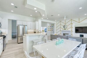 A modern kitchen with white cabinetry, a stainless steel refrigerator, and a dining area with a white table and chairs.