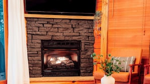 Una sala de estar acogedora con chimenea de piedra, un televisor de pantalla plana montado encima y un mobiliario cómodo.