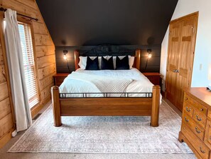 Un dormitorio con cama de madera, una mesita de noche, un aparador y una ventana con persianas.