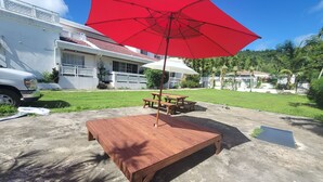 Ein Holztisch mit einem roten Sonnenschirm, einem weißen Auto und einem Haus im Hintergrund.