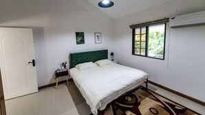 Ein Schlafzimmer mit einem Bett, einem Nachttisch, einer Wand-Klimaanlage und einem Fenster mit Blick auf Grünflächen.