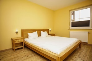 A bedroom with a wooden bed, two bedside tables, a window, and a radiator.