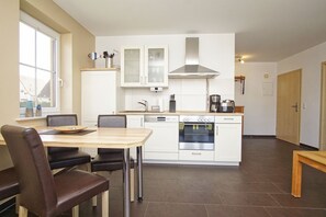 A modern kitchen with white cabinets, a stainless steel range hood, and a dining area with a wooden table and chairs.
